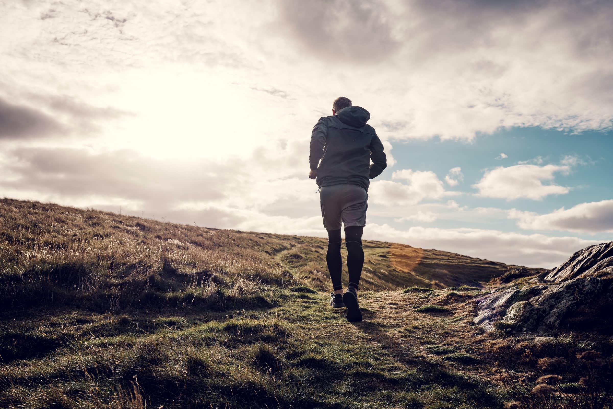 A runner heading up a grassy hill under a bright, cloudy sky